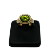 Gold ring with a green gemstone on a black stand against a white background