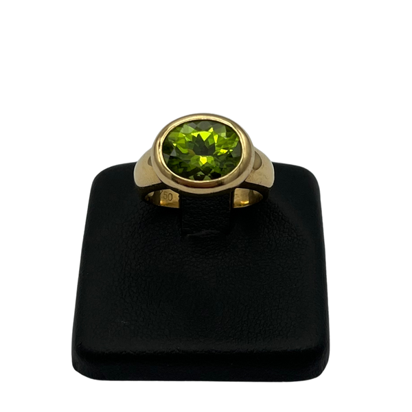 Gold ring with a green gemstone on a black stand against a white background