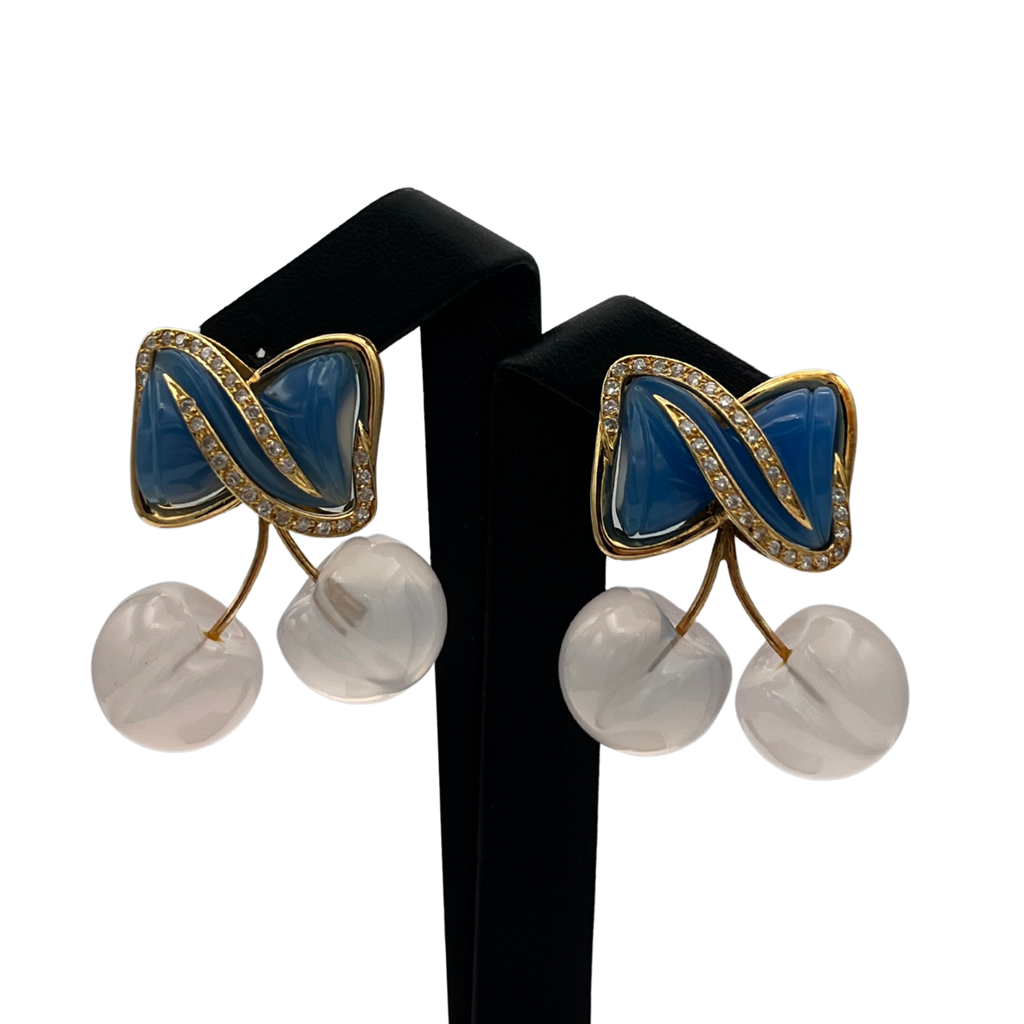 Pair of earrings with blue and pink cherries and white spherical elements on a black stand.