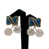 Pair of earrings with blue and pink cherries and white spherical elements on a black stand.