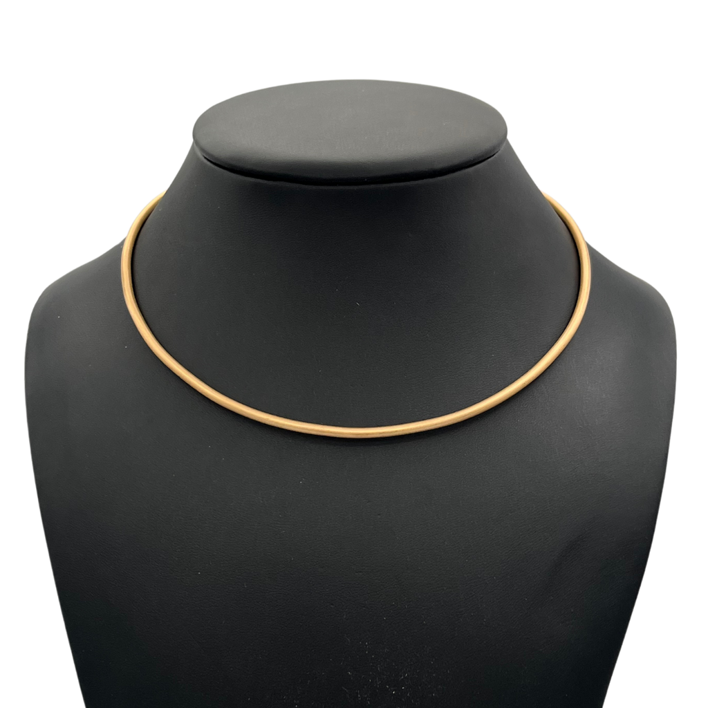 Gold necklace on a black mannequin bust against a white background